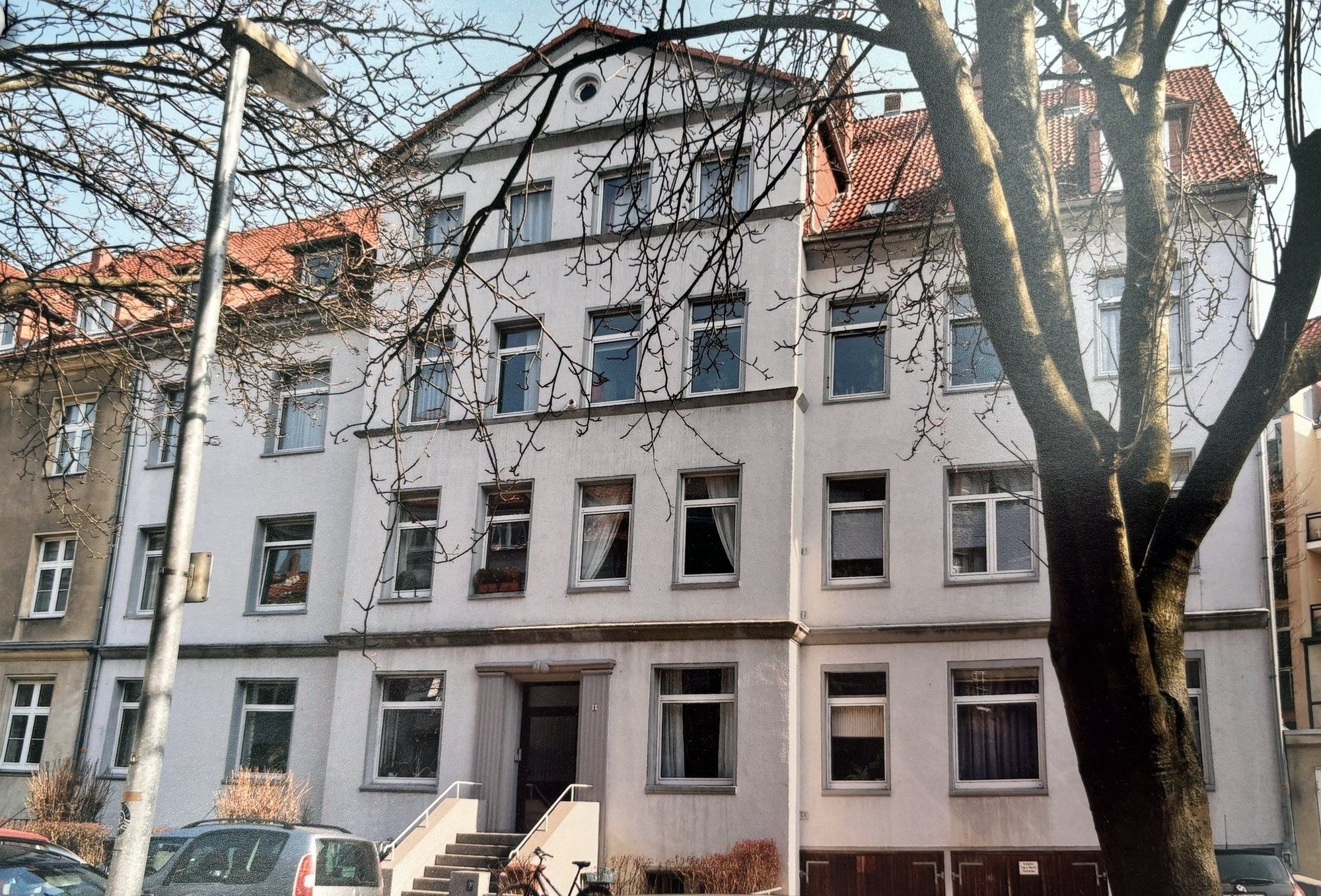 Helles Altbau-Mehrfamilienhaus Bessemerstraße 1 mit Ziergiebel und Freitreppe, davor ein großer Straßenbaum