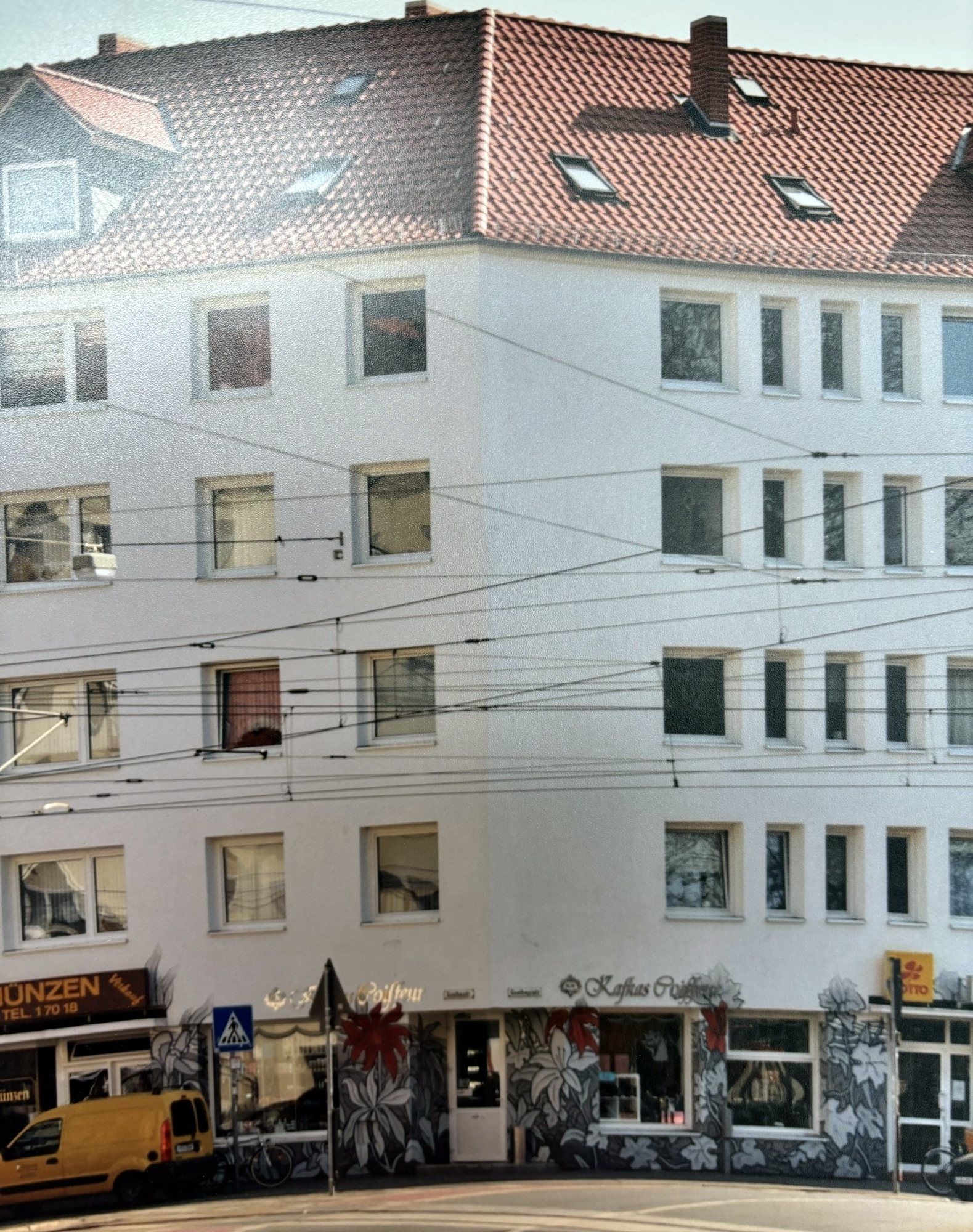 Weißes Eckhaus am Goetheplatz mit rotem Ziegeldach, Oberleitungen der Stadtbahn und bemalter Ladenfront im Erdgeschoss