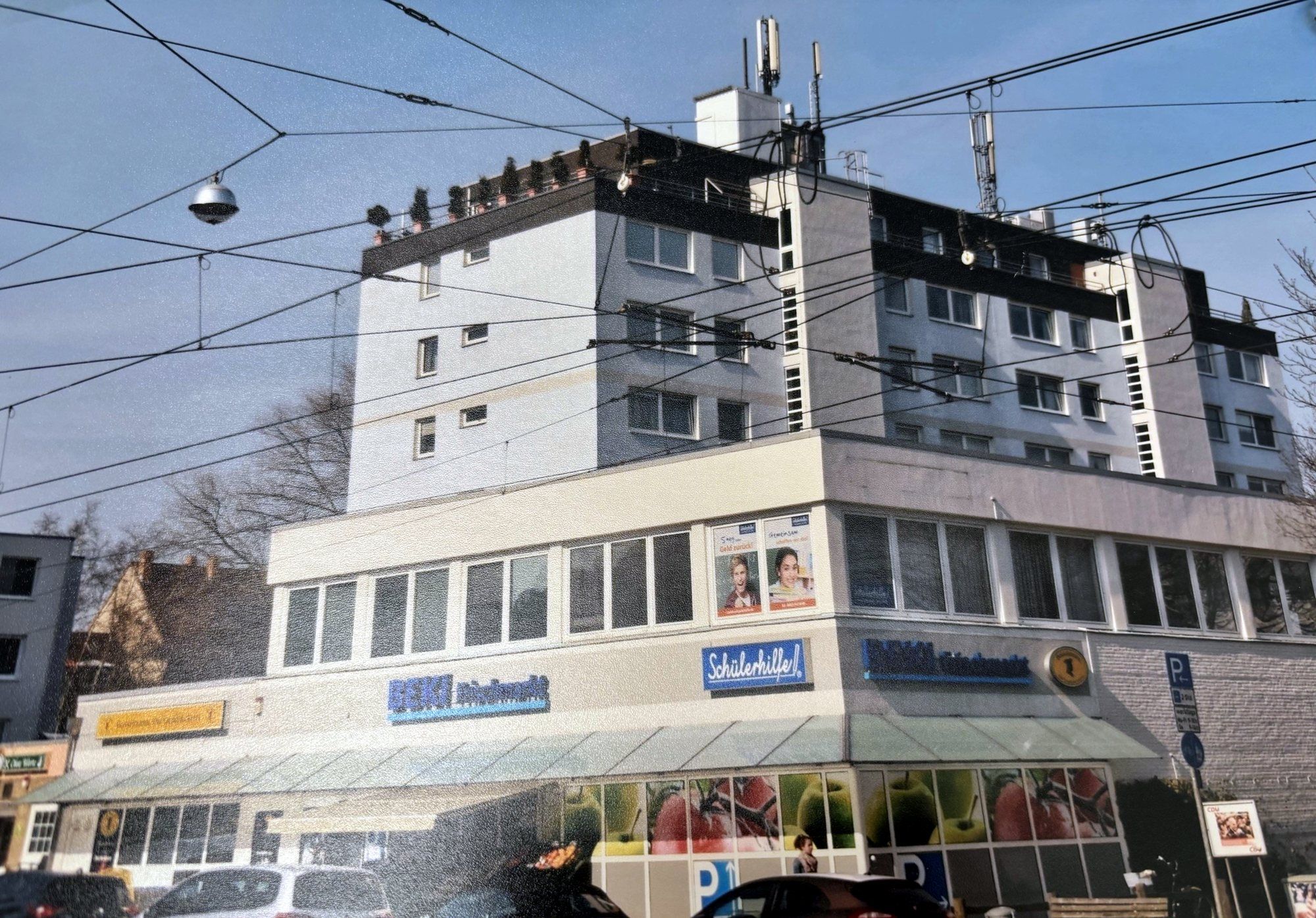 Weißes Wohnhochhaus an der Uhlhornstraße über einem zweigeschossigen Geschäftssockel, davor Oberleitungen der Stadtbahn